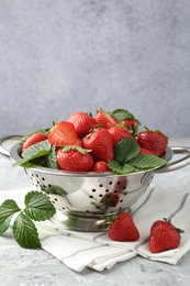 Photo of Delicious ripe strawberries and green leaves on grey table, closeup