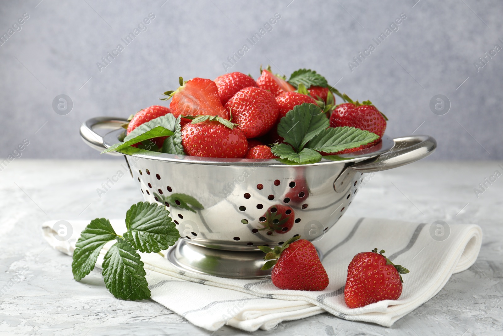 Delicious ripe strawberries and green leaves on grey table, closeup Photo of Delicious ripe strawberries and green leaves on grey table, closeup
