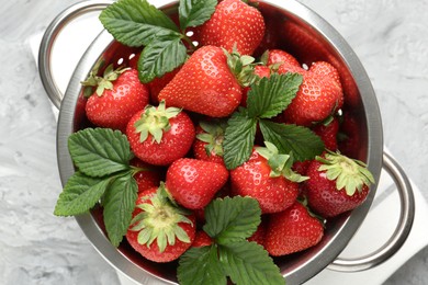 Photo of Delicious ripe strawberries and green leaves in colander on grey table, top view