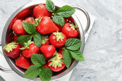 Photo of Delicious ripe strawberries and green leaves in colander on grey table, top view. Space for text