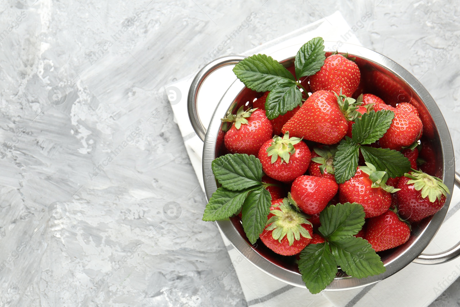 Delicious ripe strawberries and green leaves in colander on grey table, top view. Space for text Photo of Delicious ripe strawberries and green leaves in colander on grey table, top view. Space for text