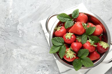 Photo of Delicious ripe strawberries and green leaves in colander on grey table, top view. Space for text