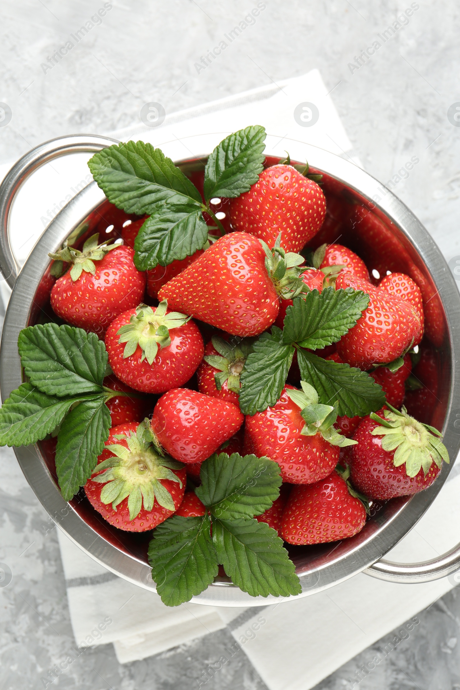 Delicious ripe strawberries and green leaves in colander on grey table, top view Photo of Delicious ripe strawberries and green leaves in colander on grey table, top view