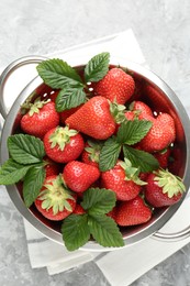 Photo of Delicious ripe strawberries and green leaves in colander on grey table, top view