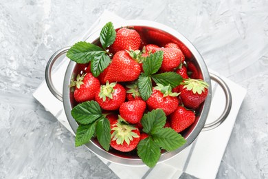Photo of Delicious ripe strawberries and green leaves in colander on grey table, top view