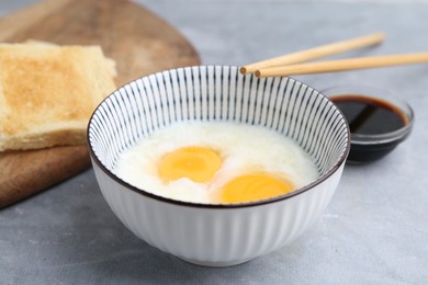 Photo of Traditional asian breakfast with half-boiled eggs in bowl, soy sauce, bread and chopsticks on grey table, closeup