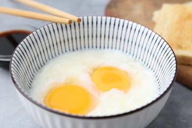 Photo of Traditional asian breakfast with half-boiled eggs in bowl, soy sauce, bread and chopsticks on grey table, closeup