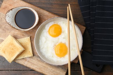 Photo of Traditional asian breakfast with half-boiled eggs in bowl, soy sauce, bread and chopsticks on wooden table, top view