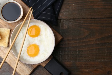 Photo of Traditional asian breakfast with half-boiled eggs in bowl, soy sauce, bread and chopsticks on wooden table, top view. Space for text