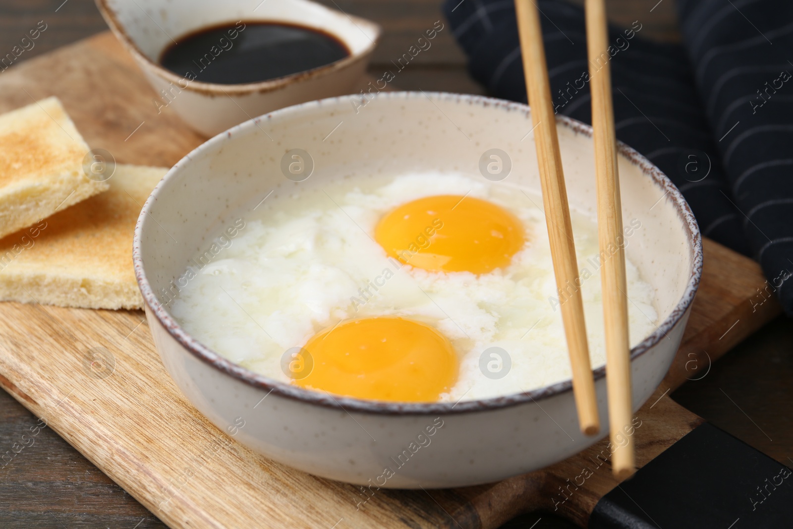 Traditional asian breakfast with half-boiled eggs in bowl, soy sauce, bread and chopsticks on wooden table, closeup Photo of Traditional asian breakfast with half-boiled eggs in bowl, soy sauce, bread and chopsticks on wooden table, closeup