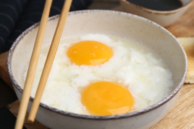 Photo of Traditional asian breakfast with half-boiled eggs in bowl, chopsticks and soy sauce on table, closeup