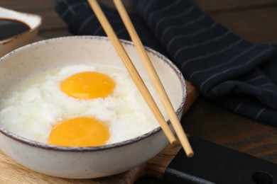 Photo of Traditional asian breakfast with half-boiled eggs in bowl, chopsticks and soy sauce on wooden table, closeup