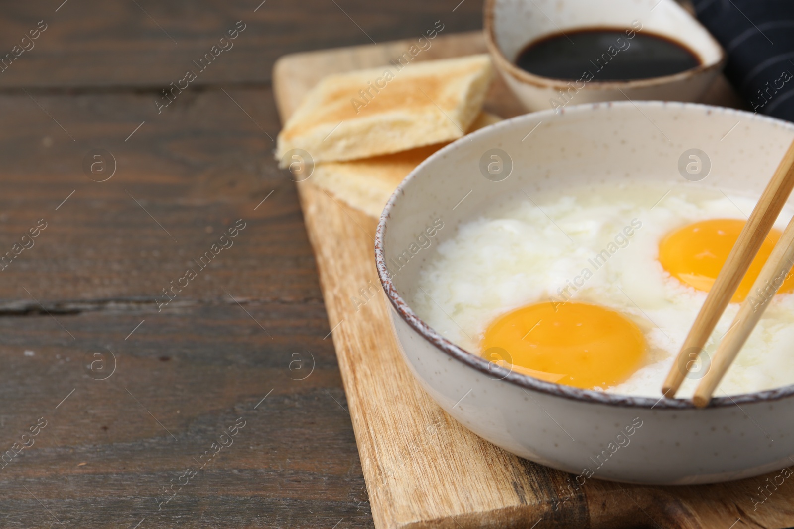 Traditional asian breakfast with half-boiled eggs in bowl, soy sauce, bread and chopsticks on wooden table, closeup. Space for text Photo of Traditional asian breakfast with half-boiled eggs in bowl, soy sauce, bread and chopsticks on wooden table, closeup. Space for text