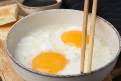 Photo of Traditional asian breakfast with half-boiled eggs in bowl, chopsticks, bread and soy sauce on table, closeup