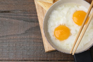 Photo of Traditional asian breakfast with half-boiled eggs in bowl, chopsticks and bread on wooden table, top view. Space for text