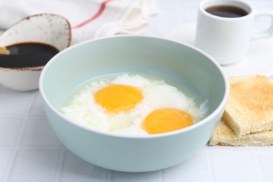 Photo of Traditional asian breakfast with half-boiled eggs in bowl, soy sauce, bread and coffee on white tiled table, closeup