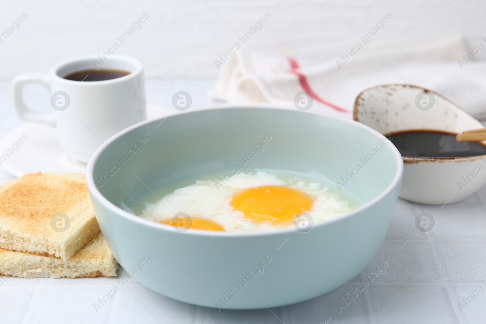 Traditional asian breakfast with half-boiled eggs in bowl, soy sauce, bread and coffee on white tiled table, closeup Photo of Traditional asian breakfast with half-boiled eggs in bowl, soy sauce, bread and coffee on white tiled table, closeup