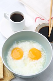 Photo of Traditional asian breakfast with half-boiled eggs in bowl, soy sauce, bread, chopsticks and coffee on white table, above view