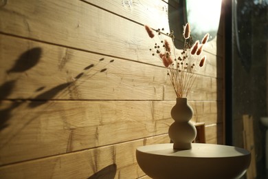 Photo of Dry flowers and spikes in vase on table near wooden wall indoors