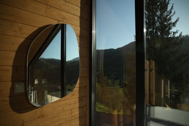 Photo of Beautiful mirror on wooden wall near window indoors