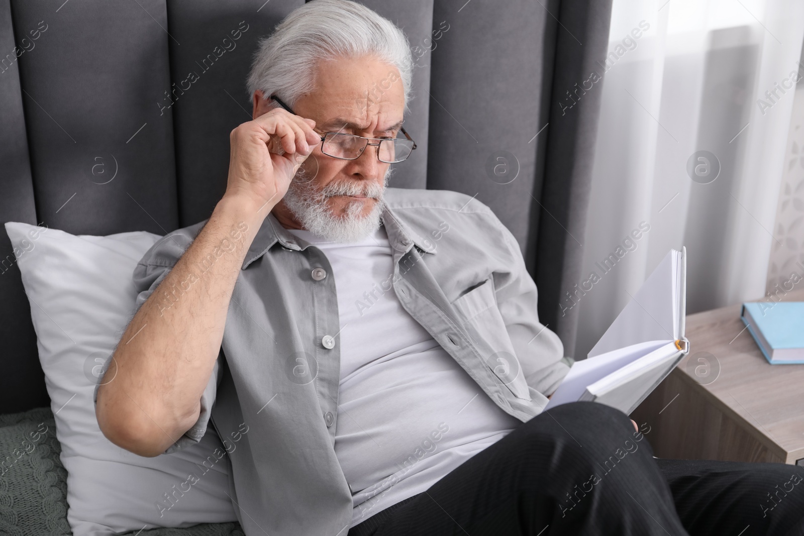 Senior man with vision problem reading book on bed at home Photo of Senior man with vision problem reading book on bed at home
