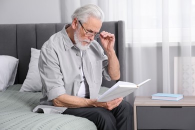 Photo of Senior man with vision problem reading book on bed at home