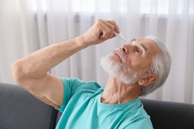Photo of Senior man applying eye drops on sofa at home