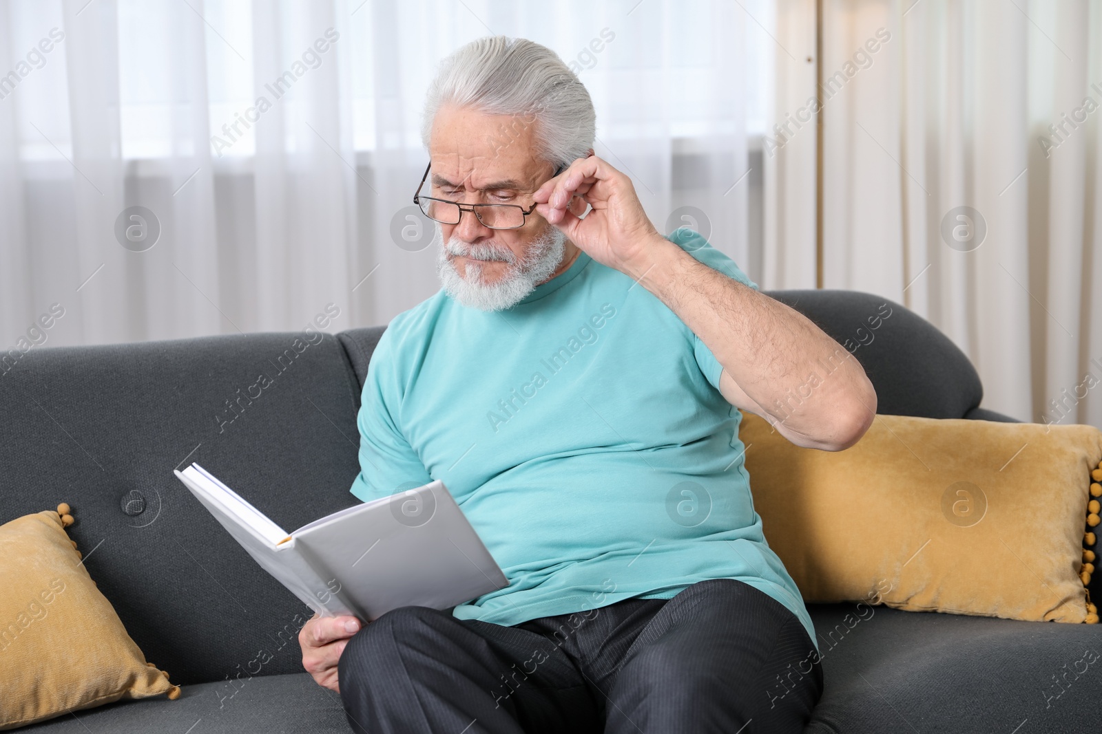 Senior man with vision problem reading book on sofa at home Photo of Senior man with vision problem reading book on sofa at home