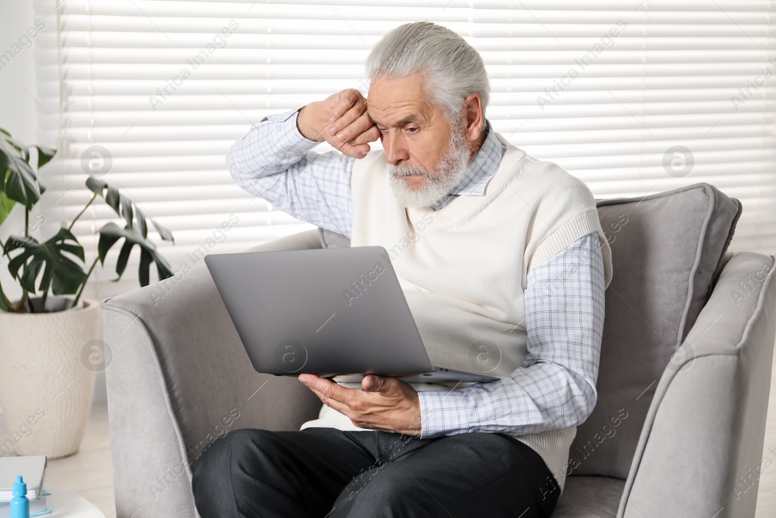 Senior man with vision problem using laptop in armchair at home Photo of Senior man with vision problem using laptop in armchair at home