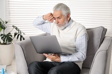 Photo of Senior man with vision problem using laptop in armchair at home