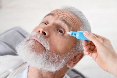 Photo of Woman dripping medication into man's eye at home, closeup