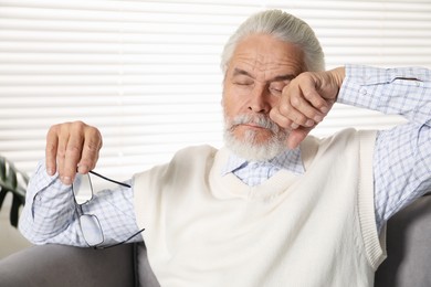 Photo of Senior man with glasses suffering from eyestrain in armchair at home