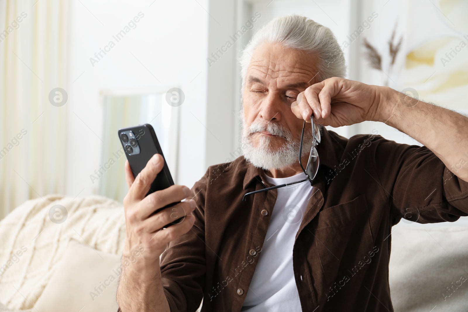 Senior man with vision problem using smartphone on sofa at home Photo of Senior man with vision problem using smartphone on sofa at home
