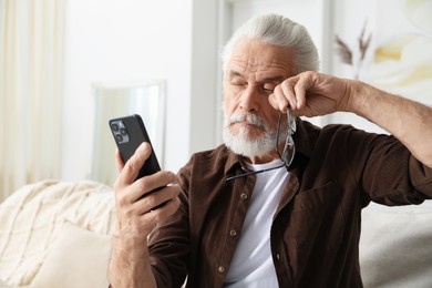 Photo of Senior man with vision problem using smartphone on sofa at home
