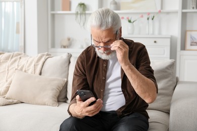 Photo of Senior man with vision problem using smartphone on sofa at home