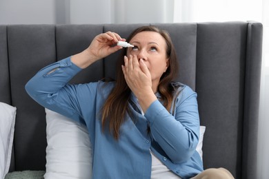 Photo of Woman applying eye drops on bed at home