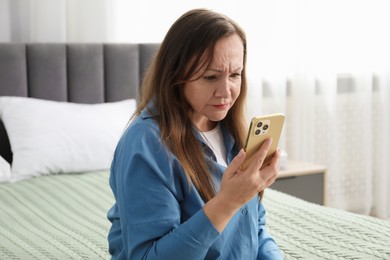 Photo of Woman with vision problem using smartphone on bed at home