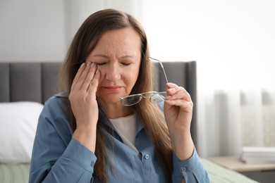 Photo of Woman with glasses suffering from eyestrain on bed at home