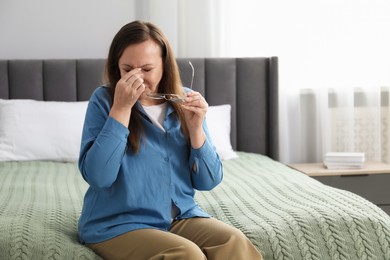 Photo of Woman with glasses suffering from eyestrain on bed at home, space for text