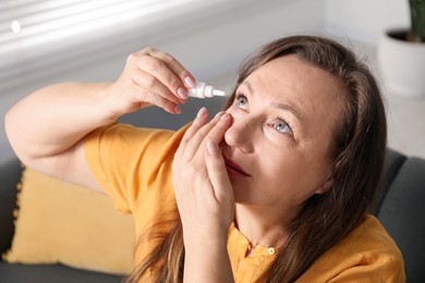 Photo of Woman applying eye drops on sofa at home