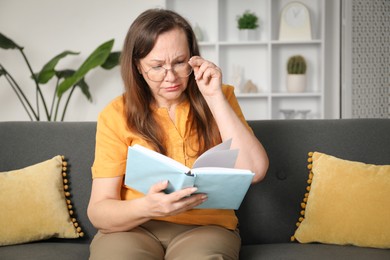 Photo of Woman with vision problem reading book on sofa at home