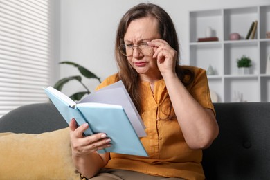 Photo of Woman with vision problem reading book on sofa at home