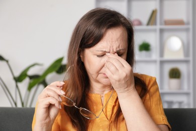 Photo of Woman with glasses suffering from eyestrain on sofa at home