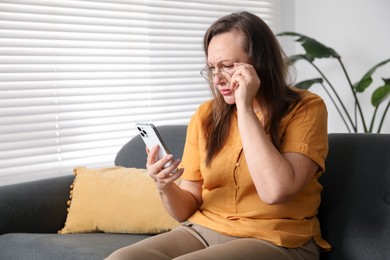 Photo of Woman with vision problem using smartphone on sofa at home, space for text