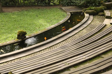 Photo of Wooden benches, water canal with golden fishes and green lawn outdoors