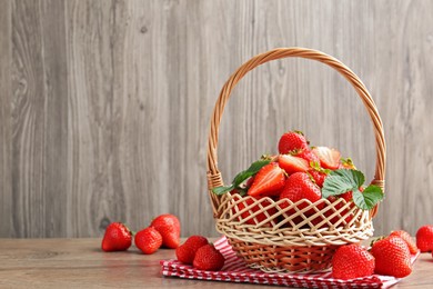 Photo of Delicious ripe strawberries in wicker basket on wooden table, space for text