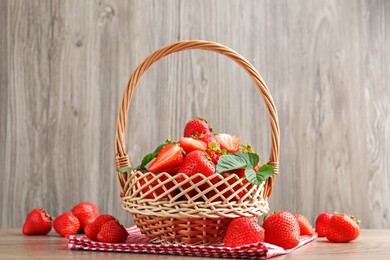 Photo of Delicious ripe strawberries in wicker basket on wooden table