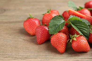 Photo of Delicious ripe strawberries and green leaves on wooden table, closeup. Space for text
