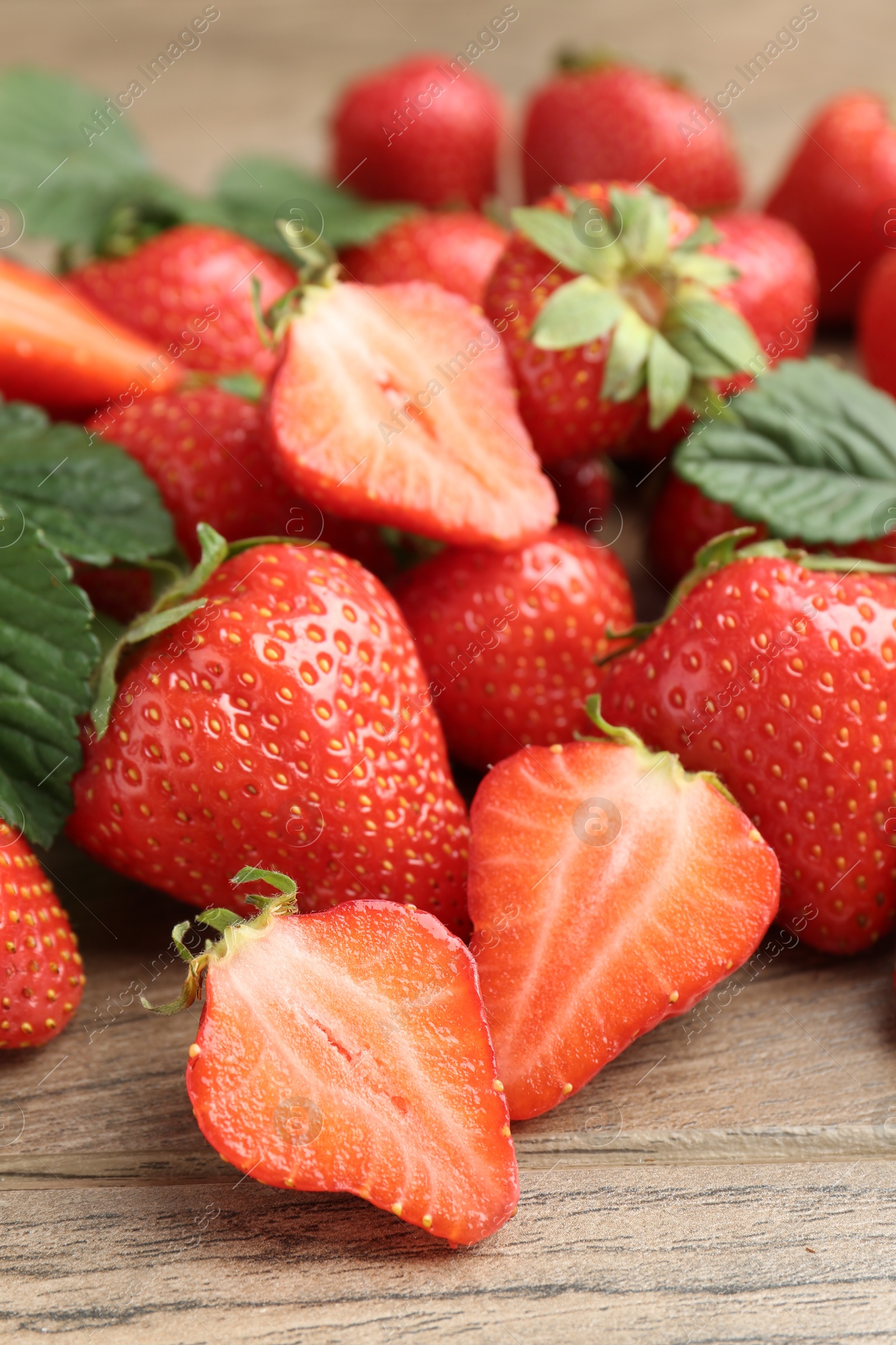 Delicious ripe strawberries and green leaves on wooden table, closeup Photo of Delicious ripe strawberries and green leaves on wooden table, closeup