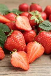 Photo of Delicious ripe strawberries and green leaves on wooden table, closeup